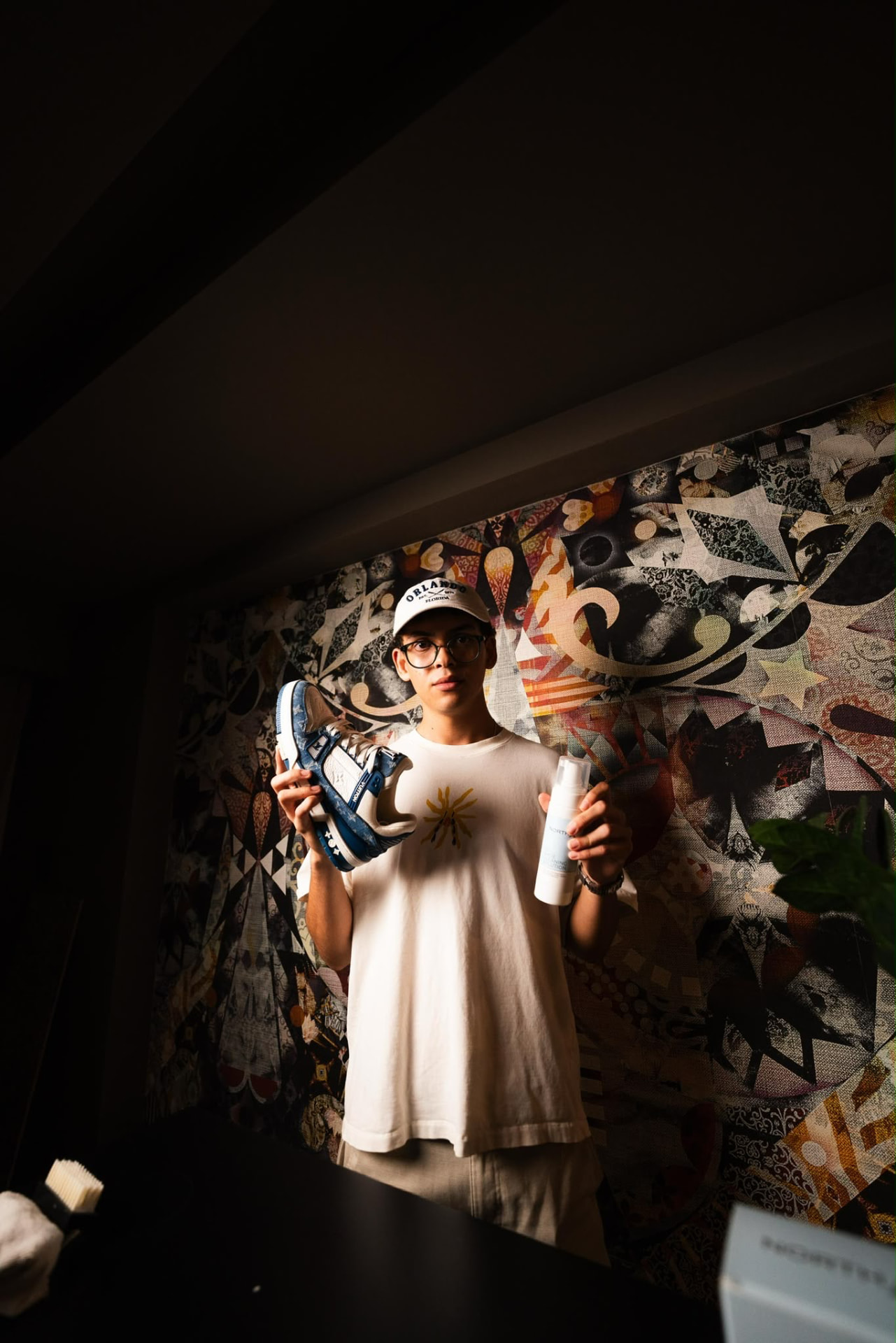 Ryan Sabik holding up a blue-and-white sneaker and a bottle of sneaker cleaner in front of a patterned wall